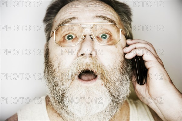 Senior with a full beard and glasses in undershirt on the smartphone