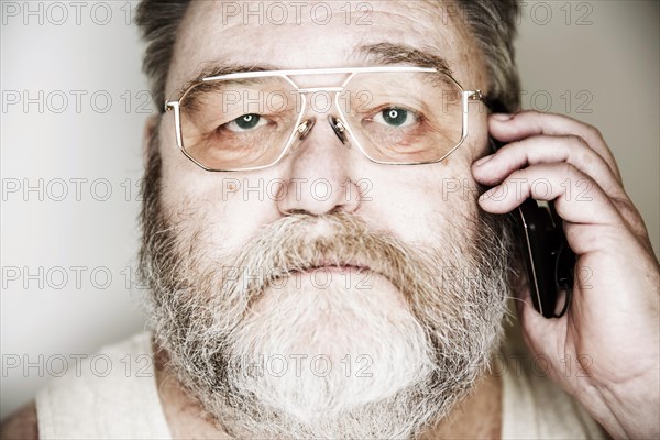 Senior with a full beard and glasses in undershirt on the smartphone