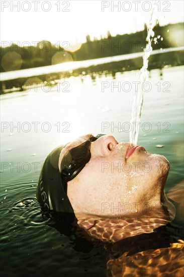 Man with swimming goggles spitting water in lake