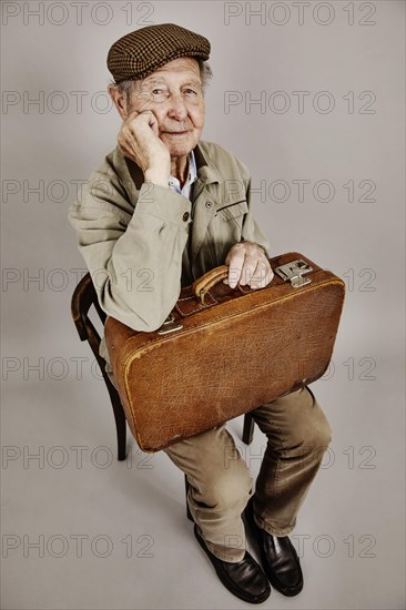 Senior sits with old suitcase on a chair