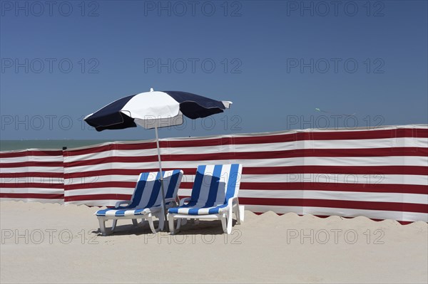 Two empty sun-beds behind a windbreak