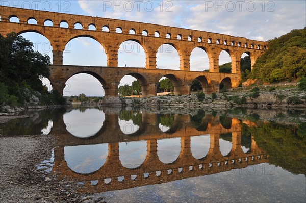 Roman aqueduct Pont du Gard reflected in the Gardon river in the evening