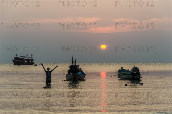 Young man in water with two long-tail boats