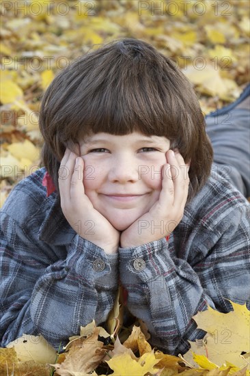 Little boy lying in autumn leaves