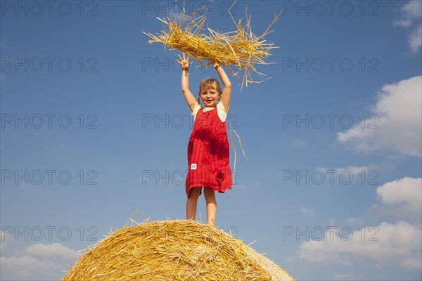 Little girl standing on a bale of straw throwing straw