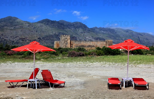Red sun loungers and parasols in front of Frangokastello castle