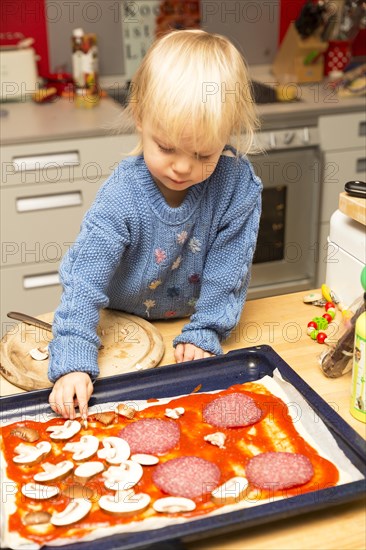 Toddler topping a pizza