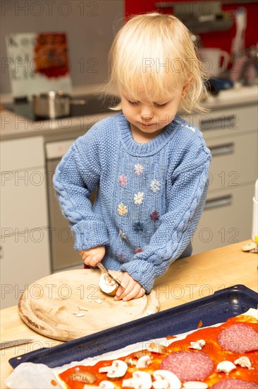 Toddler cutting things and topping a pizza