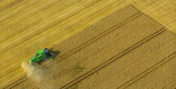 Combine harvester with dust spewing out on a corn field
