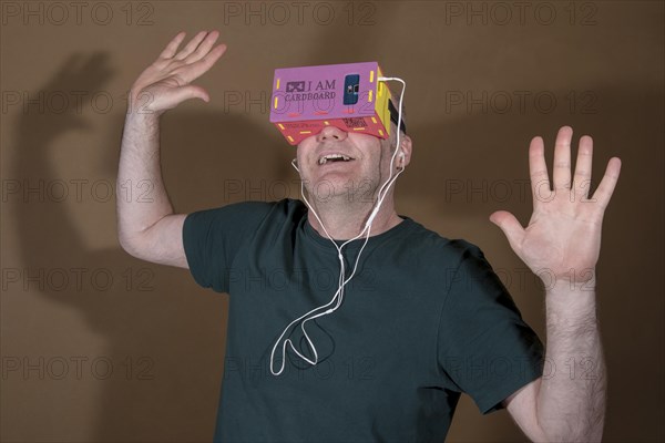 Man wearing I AM CARDBOARD 45mm focal length virtual reality Google cardboard VR goggles with Samsung Galaxy S5 Android smartphone and in-ear headphones