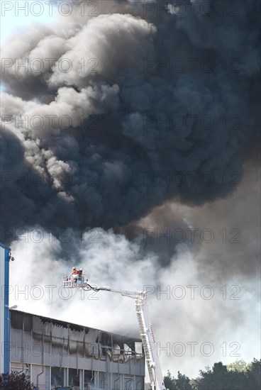Firemen on aerial ladder platform in front of big cloud of smoke