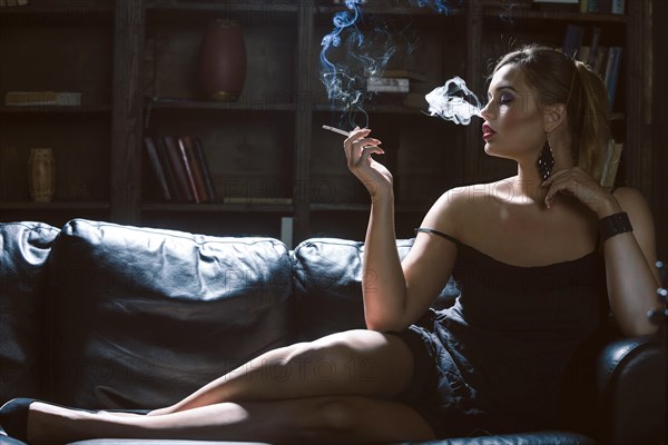 Young woman smoking a cigarette on a dark sofa