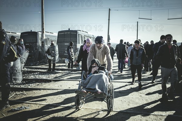 Refugees and old woman in a wheelchair on the border fence