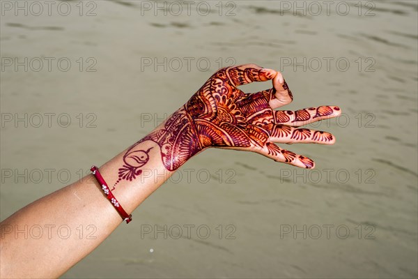 A henna painted hand is showing the mudra "Gyan Mudra" at the ghats of the holy river Ganges
