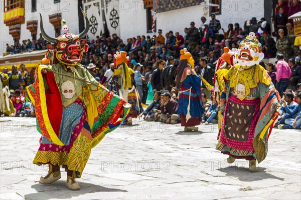 Monks with big wooden masks and colorful costumes are performing ritual dances at Hemis Festival in the courtyard of the monastery