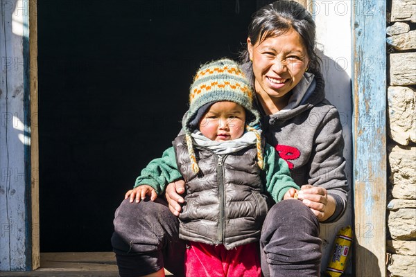 Portrait of a smiling young nepali mother with her child sitting in a doorway