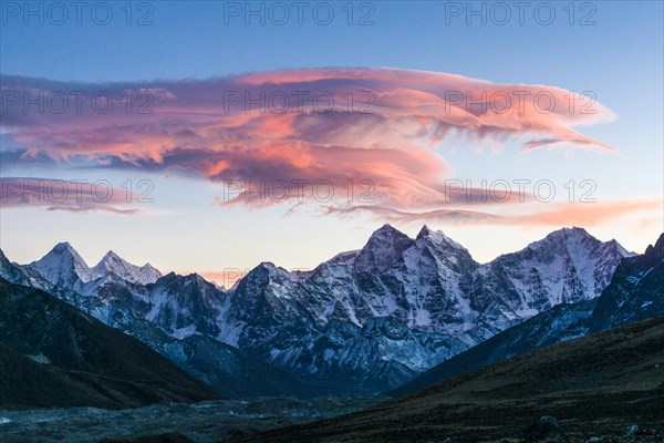 Big pink cloud over a snow covered mountain range at sunset