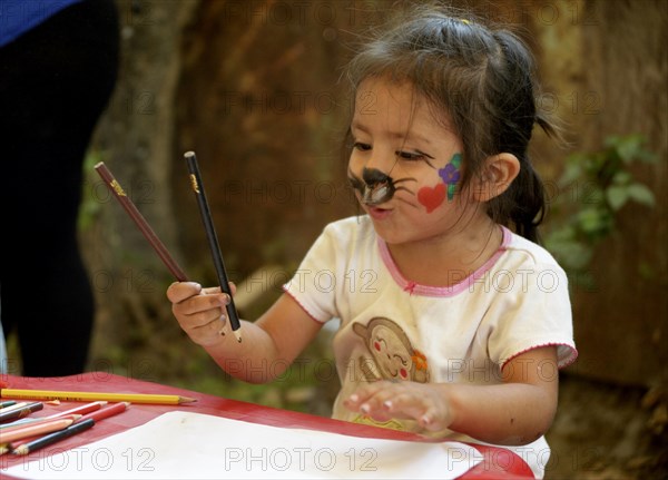 Girl with face painted as a cat drawing at a children's festival