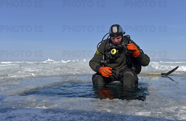 Ice diver by an ice hole preparing to dive