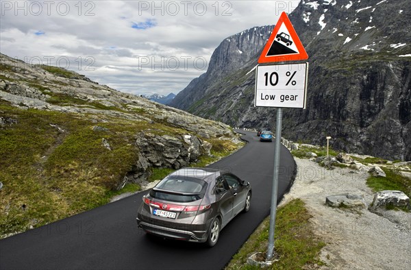 Cars by a warning sign in front of a steep slope