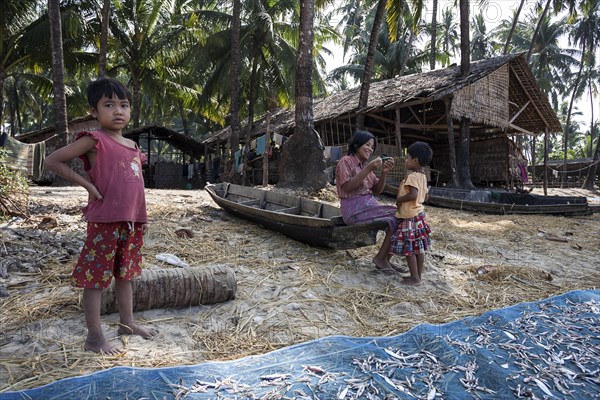 Native woman and two children in front of a wooden house of a fisherman on the beach