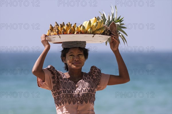 Native woman with a bowl of bananas on her head and Thanaka paste on her face