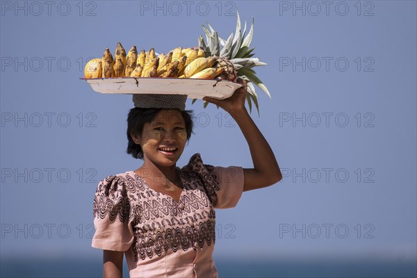 Native woman with a bowl of bananas on her head and Thanaka paste on her face