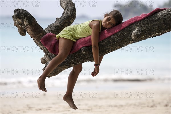 Local girl lying on tree branch on Beau Vallon beach