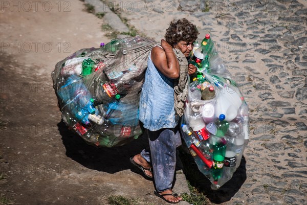 Elderly woman carrying bags with plastic bottles to sell for recycling