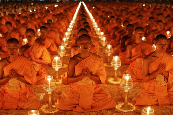 Monks sitting in rows praying and meditating by candlelight