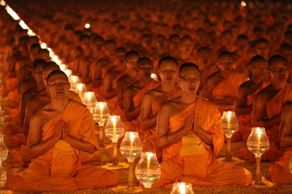 Monks sitting in rows praying and meditating by candlelight