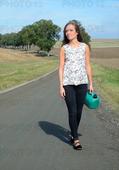 Young brunette with petrol can walking on country road