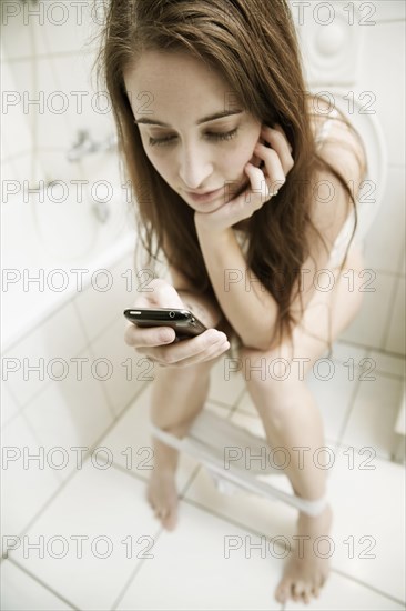 Young woman with mobile phone on the toilet