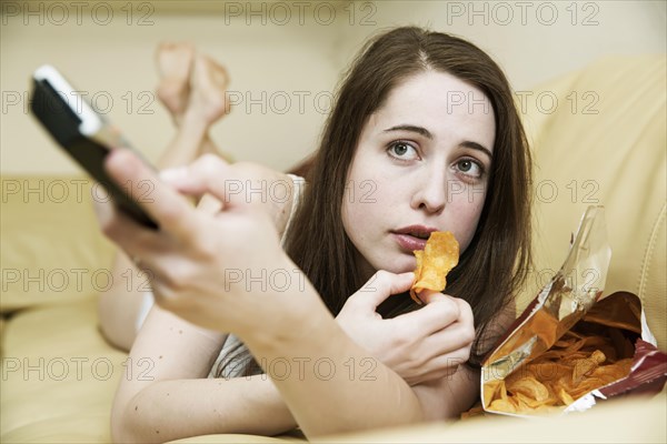 Young woman in underwear watching TV on the sofa with a bag of chips and the remote control in hand