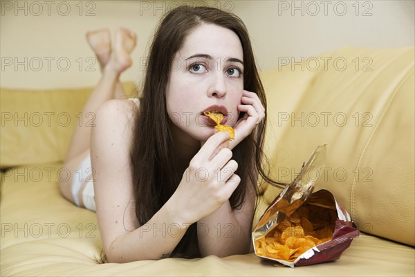 Young woman in underwear on the sofa with a bag of chips