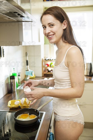 Young woman in underwear is preparing eggs for breakfast in the kitchen