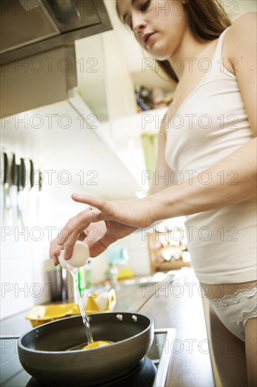 Young woman in underwear is preparing eggs for breakfast in the kitchen