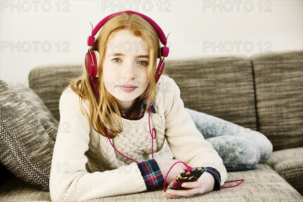 Girl lying on the sofa and listening to music with headphones and a smartphone
