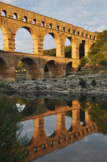 Roman aqueduct Pont du Gard reflected in the Gardon river in the evening