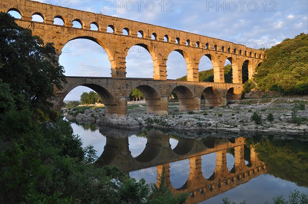 Roman aqueduct Pont du Gard reflected in the Gardon river in the evening