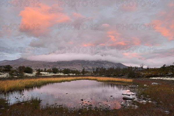 Red sky and mist in the morning above the peaks of the Stygghoin or Stygghoin mountain group reflected in a small lake