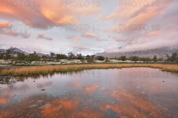 Red sky and mist in the morning above the peaks of the Stygghoin or Stygghoin mountain group reflected in a small lake