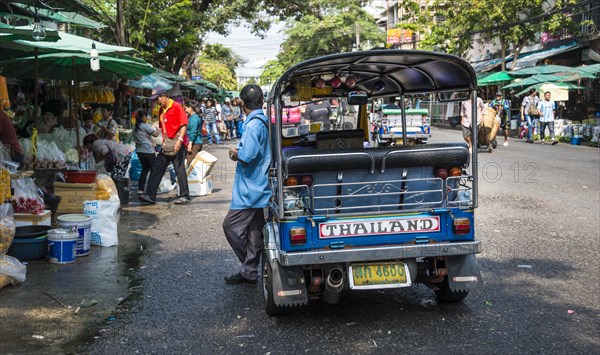 Tuk-tuk driver waiting by his car on busy road