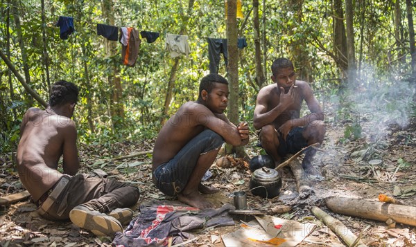 Three young aboriginal Orang Asil men sitting on the ground in the jungle