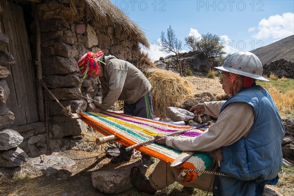 Old Indio man with helmet weaving a colorful rug with a simple loom