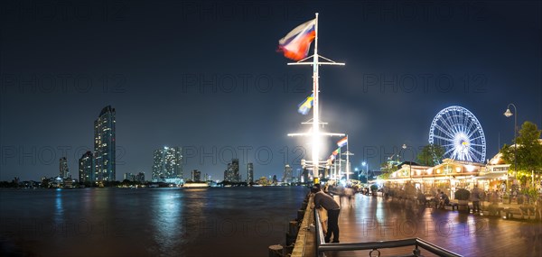 River promenade in the evening with a Ferris wheel and the skyline on the river Mae Nam Chao Phraya