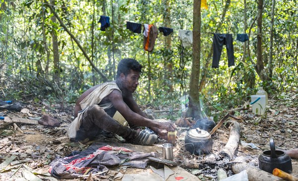 Young man of the Orang Asil tribe sitting on the floor in the jungle and making tea