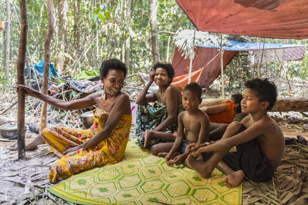 Women and children of the Orang Asil tribe sitting under tarpaulins in the jungle