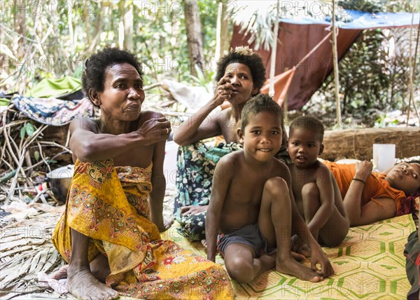 Women and children of the Orang Asil tribe sitting under tarpaulins in the jungle