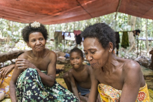 Women and children of the Orang Asil tribe sitting under tarpaulins in the jungle